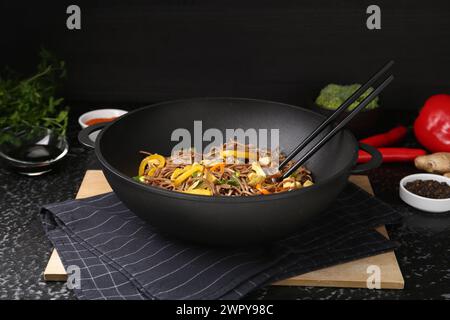 Friggere in padella. Gustosi spaghetti con verdure, carne e bacchette nel wok su un tavolo con superficie scura Foto Stock