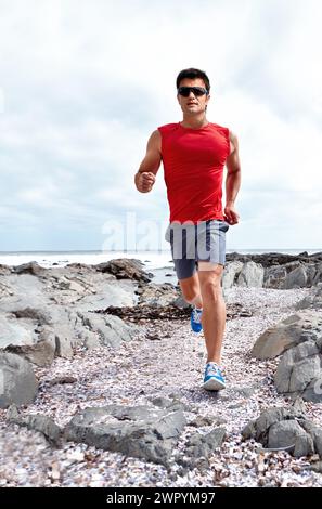 Atleta uomo, corsa e spiaggia per fitness, salute e benessere in abbigliamento sportivo e occhiali da sole. Uomo, jogging e mare per sport, allenamento e.. Foto Stock