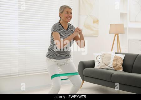 Donna anziana che fa gli squat con fascia elastica fitness a casa Foto Stock