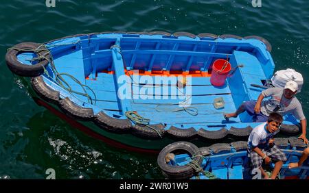 Pescatore locale e suo figlio sulla sua barca in legno dipinto blu in attesa di portare a terra i passeggeri da una nave che cambia equipaggio in Perù, Foto Stock