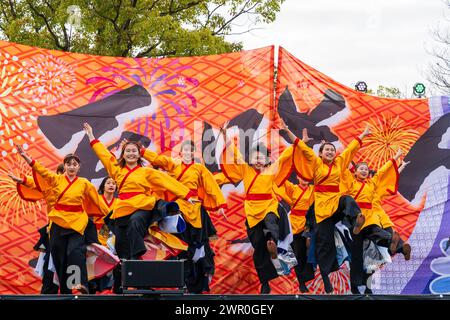 Ragazze adolescenti giapponesi della squadra di danza Yosakoi in yukata arancione e pantaloni neri che ballano su un palco all'aperto al festival Kumamoto Kyusyu Gassai. Foto Stock