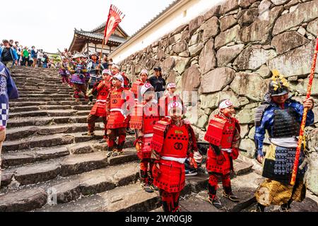 Giovani ragazze giapponesi vestite di armatura rossa come soldati ashigaru in attesa sui gradini del castello di pietra a Tatsuno durante la parata dei samurai in primavera Foto Stock