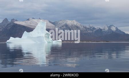 Il grande iceberg Groenlandia Nanortalik galleggia nel tranquillo fiordo di mare artico con montagne innevate riflesse sullo sfondo Foto Stock