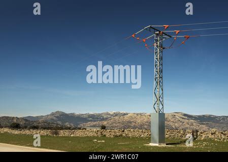 una strada sterrata rurale fiancheggiata da campi erbosi, una catena montuosa e una linea elettrica su pali sopraelevati Foto Stock