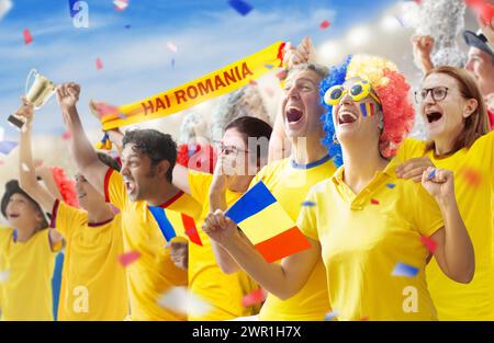 Tifoso di calcio rumeno nello stadio. Tifosi rumeni sul campo di calcio guardando la squadra giocare. Gruppo di tifosi con bandiera e maglia nazionale che tira Foto Stock