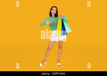 Giovane donna gioiosa che punta la borsa della spesa in mano Foto Stock