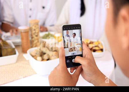 Uomo che scatta foto di famiglia asiatica e amico che celebra la festa di Eid Mubarak con cibo sulla tavola Foto Stock