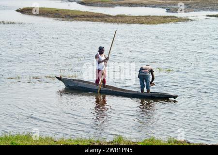 Due abitanti del villaggio che pescano da una canoa in una laguna di un fiume in Africa; uno sta colpendo la barca e uno sta lanciando la rete da pesca Foto Stock