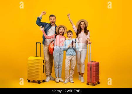 Famiglia felice di quattro persone con valigie e biglietti in posa su sfondo giallo Foto Stock
