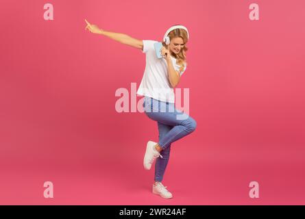 Allegra bionda signora posa felicemente con telefono e cuffie, studio Foto Stock