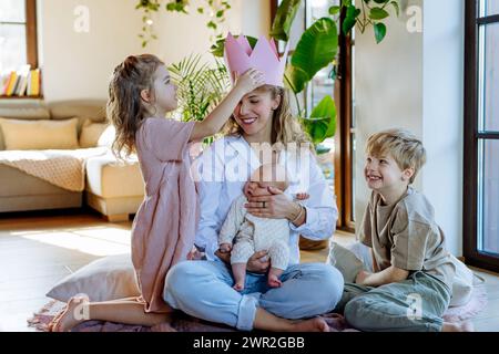 Madre dopo aver partorito come regina. Figlia che dà alla mamma una corona di carta, ammirazione, amore per le madri, concetto di festa della mamma e forza delle donne. Foto Stock