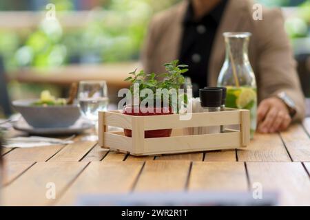 Tavolo in legno sul patio del ristorante. Tavolo da pranzo con sale, spezie, contenitori per condimenti in cassa, piccola pianta come decorazione. Foto Stock