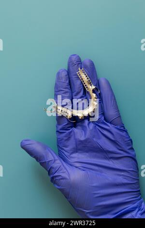 Metal Frame Lower Partial Denture, piastra dentaria cromata cobalto, ponte stampato da stampante 3d in mano al medico. Sfondo blu. Flat Lay Mockup. Copia Foto Stock