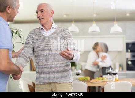 Due uomini sorrisero e si salutarono con una stretta di mano prima di prendere posto a un tavolo da pranzo splendidamente allestito Foto Stock