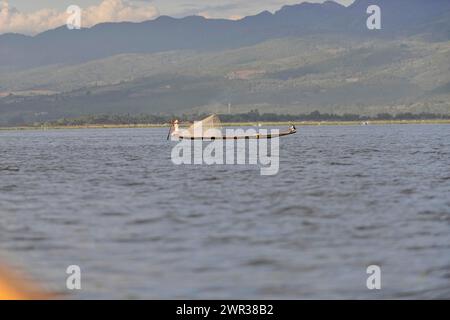 Pescatore solitario su una barca che tira una rete in acque calme, lago Inle, Myanmar Foto Stock