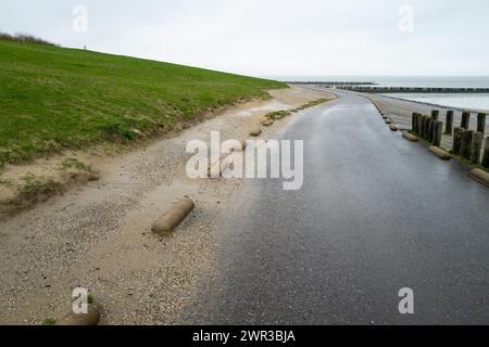 Percorso costiero bagnato accanto a un'area erbosa e sabbia con un cielo nuvoloso, Breskens, Zelanda, Paesi Bassi Foto Stock