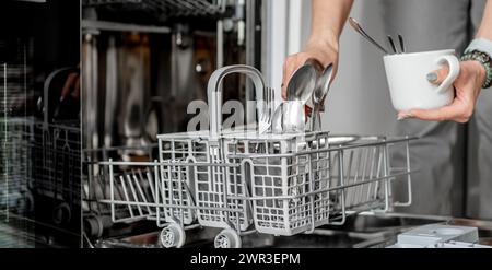 La giovane donna sta caricando i cucchiai in lavastoviglie in vista ravvicinata Foto Stock