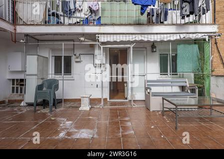 Cortile interno di una casa con pavimenti in terracotta scura, una recinzione libica in alluminio, alcuni mobili sparsi e balconi con abiti appesi sulla u Foto Stock