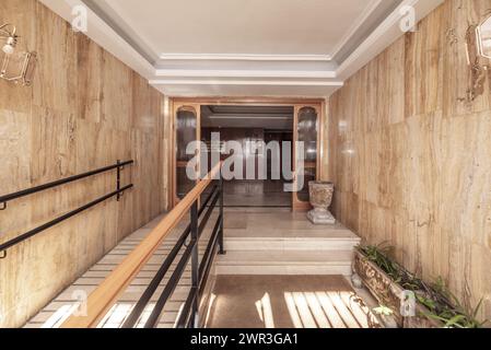 Portale di accesso ad un edificio residenziale di appartamenti con pareti rivestite in marmo, ringhiere con corrimano in legno e marmo bianco sulle scale Foto Stock
