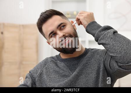 Giovane uomo che applica gocce di orecchio medico in casa Foto Stock