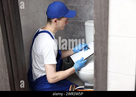 Giovane idraulico che scrive i risultati dell'esame della ciotola del water nell'armadio ad acqua Foto Stock