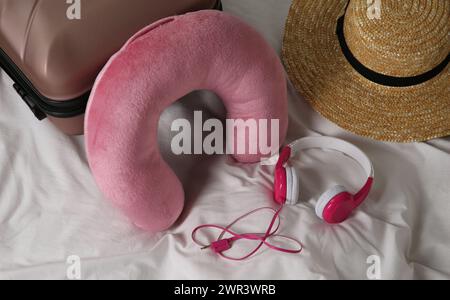 Cuscino da viaggio rosa, valigia, cappello e cuffie sul letto Foto Stock