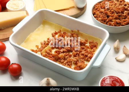 Cottura delle lasagne. Fogli di pasta, carne macinata nel vassoio da forno e prodotti su tavola bianca, primo piano Foto Stock