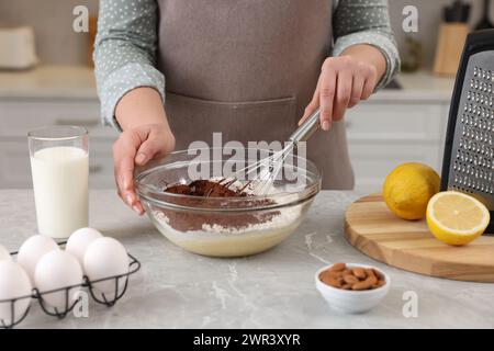 Donna che prepara l'impasto al cioccolato con la frusta nel recipiente al tavolo di marmo grigio, primo piano Foto Stock