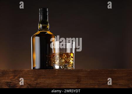 Whisky con cubetti di ghiaccio in vetro e bottiglia su un tavolo in legno, vista ad angolo basso. Spazio per il testo Foto Stock