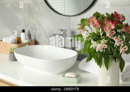 Vaso con bellissimi fiori dell'Alstroemeria e articoli da toeletta vicino al lavandino in bagno Foto Stock