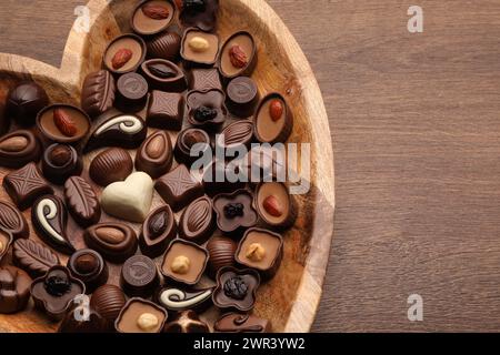 Piatto a forma di cuore con deliziose caramelle al cioccolato su un tavolo in legno, vista dall'alto Foto Stock