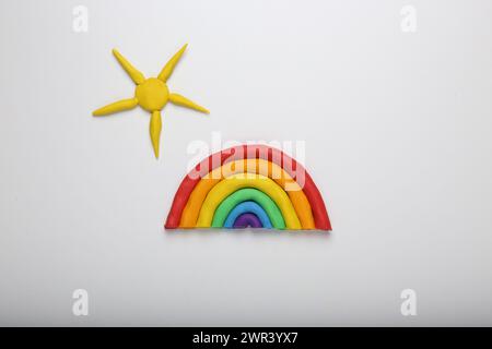 Arcobaleno e sole in plasticina su sfondo bianco, vista dall'alto Foto Stock