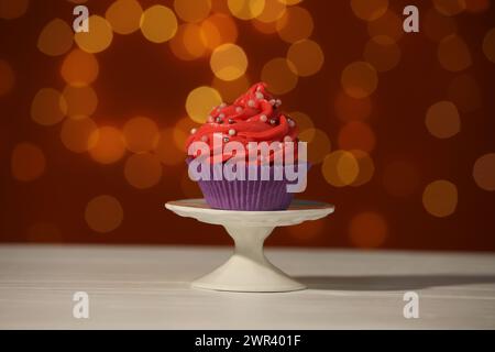 Mettiti in piedi con un gustoso cupcake sul tavolo bianco contro le luci sfocate Foto Stock