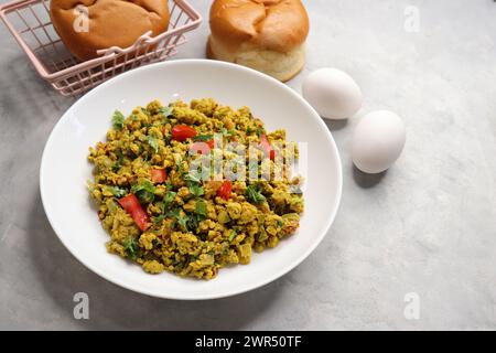 Anda Masala Bhurji o uova strapazzate indiane piccanti con pane o Bun Pav, un popolare cibo di strada a Mumbai. Serviti in un piatto bianco con spazio per le copie Foto Stock