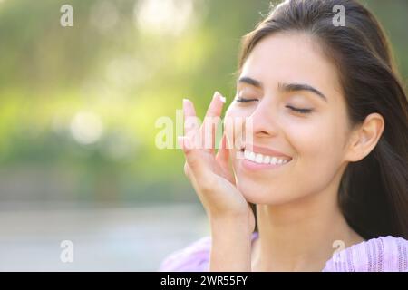 Donna di bellezza che applica crema idratante sul viso in un parco Foto Stock