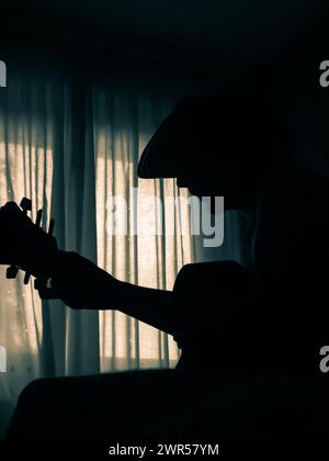 Ragazzo che suona la chitarra in una stanza buia. Bel contrasto e profilo dell'uomo che suona la chitarra e fa musica e canta. Atmosfera rilassante. Foto Stock