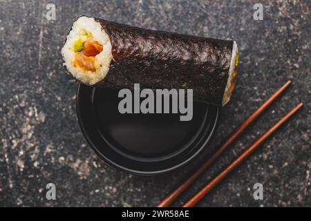 Un piatto nero con pezzi di sushi con bacchette e ciotola di salsa di soia. Il sushi mostra una varietà di colori, texture e ripieni, in vetrina Foto Stock