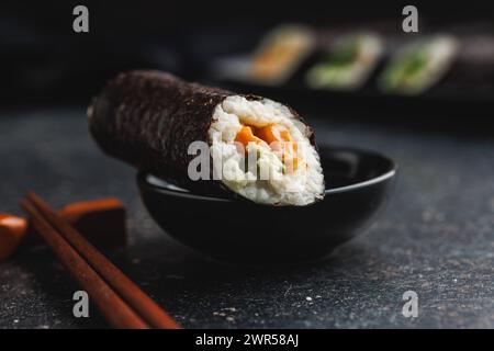 Un piatto nero con pezzi di sushi con bacchette e ciotola di salsa di soia. Il sushi mostra una varietà di colori, texture e ripieni, in vetrina Foto Stock