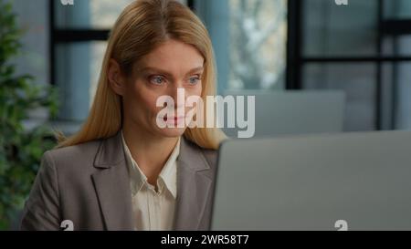 Donna caucasica di mezza età in ufficio con un computer che lavora online occupata con lavoro su Internet. Ritratto d'affari donna d'affari in azienda Foto Stock