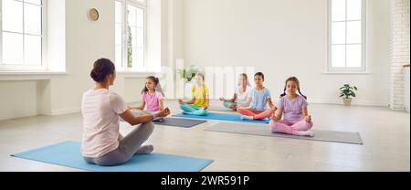 Gruppo di bambini con istruttore seduto su materassini, facendo yoga e mediazione Foto Stock