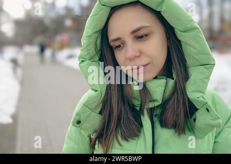 Una donna che indossa una giacca verde si trova nel terreno innevato, circondato da paesaggi bianchi Foto Stock