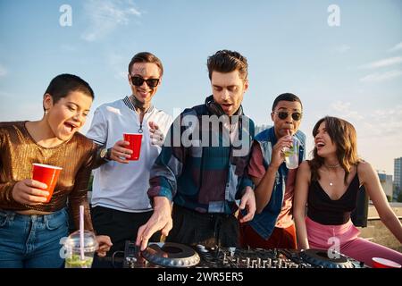 Persone interrazziali gioiose in abiti vivaci che festeggiano insieme accanto a un bel DJ alla festa sul tetto Foto Stock