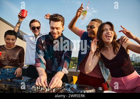 Amici interrazziali dall'aspetto allegro e simpatico in abiti urbani che festeggiano insieme a un bel DJ alla festa Foto Stock