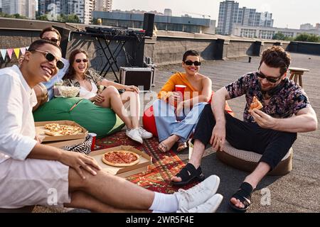 allegri amici multiculturali in abiti vivaci con occhiali da sole, pizza e bevande alla festa Foto Stock