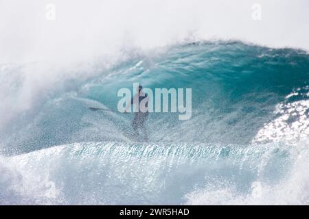 Un giovane che cavalca un'onda enorme, fai surf in piedi al Pipeline, sulla riva nord. Foto Stock