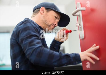 uomo che installa viti in una porta di legno Foto Stock