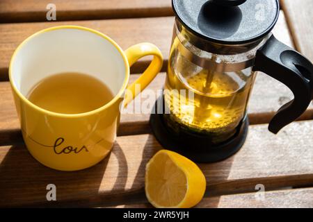 Teiera (pressa francese) con mezzo limone e teiera al tavolo di legno sul balcone, tè mattutino, aromaterapia aromatica fresca ed erboristica, tè biologico Foto Stock