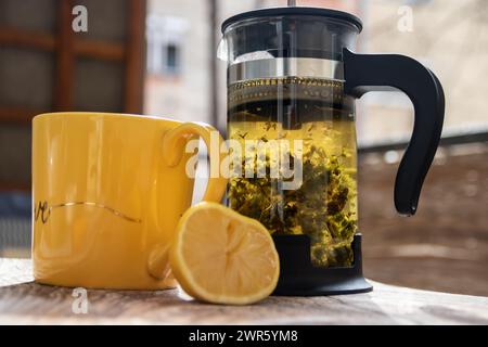 Teiera (pressa francese) con mezzo limone e teiera al tavolo di legno sul balcone, tè mattutino, aromaterapia aromatica fresca ed erboristica, tè biologico Foto Stock
