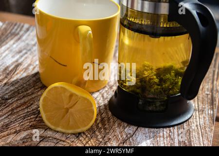 Teiera (pressa francese) con mezzo limone e teiera al tavolo di legno sul balcone, tè mattutino, aromaterapia aromatica fresca ed erboristica, tè biologico Foto Stock