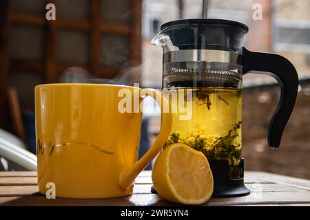 Teiera (pressa francese) con mezzo limone e teiera al tavolo di legno sul balcone, tè mattutino, aromaterapia aromatica fresca ed erboristica, tè biologico Foto Stock